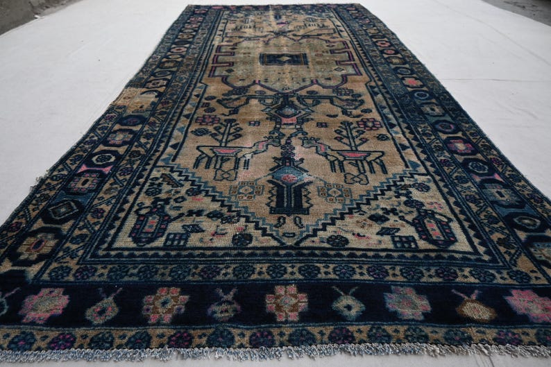 Peut inclure: Tapis ancien avec un champ central beige et une bordure bleu marine. Le tapis pr&eacute;sente des motifs complexes, notamment des motifs floraux et g&eacute;om&eacute;triques, avec des accents de rose et de bleu. Le tapis est de forme rectangulaire et a une bordure frang&eacute;e.