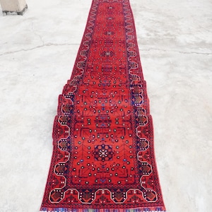 May include: A red runner rug with a traditional Persian design. The rug is rolled up and has a fringe on the ends.
