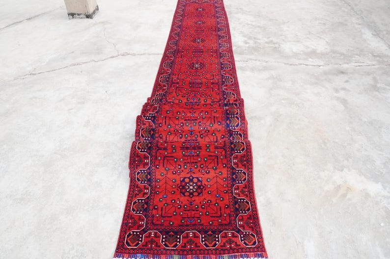 May include: A red runner rug with a traditional Persian design. The rug is rolled up and has a fringe on the ends.