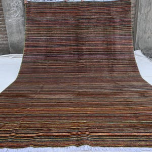 Pode incluir: Um tapete retangular longo com um padr&atilde;o listrado em tons de marrom, vermelho, verde e amarelo. O tapete tem uma borda de franjas brancas.
