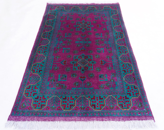 Könnte beinhalten: Ein rechteckiger magentafarbener Teppich mit türkisfarbenem Rand und komplizierten geometrischen Mustern. Der Teppich hat ein zentrales Design mit einem sich wiederholenden Blumenmotiv und einem Fransenrand. Der Teppich ist aus weichem Material.