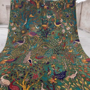 以下が含まれることがあります： 木、鳥、花の詳細なパターンが施された、大きな緑色のラグ。ラグには、クジャク、ツル、その他のエキゾチックな種を含む、さまざまなカラフルな鳥が描かれています。デザインは複雑で、ラグは柔らかい素材で作られているようです。