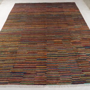 May include: A rectangular area rug featuring a dense, multi-colored horizontal striped pattern. The design consists of thin, alternating bands in shades of deep red, orange, yellow, blue, green, and purple, finished with a white fringe at the edge.