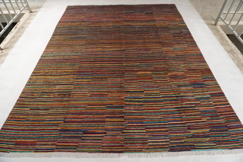 May include: A rectangular area rug featuring a dense, multi-colored horizontal striped pattern. The design consists of thin, alternating bands in shades of deep red, orange, yellow, blue, green, and purple, finished with a white fringe at the edge.