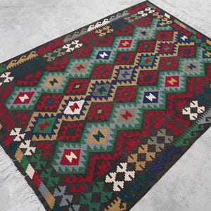May include: A colorful rug with a geometric pattern in shades of red, green, blue, and brown. The rug has a diamond pattern with a fringe border.