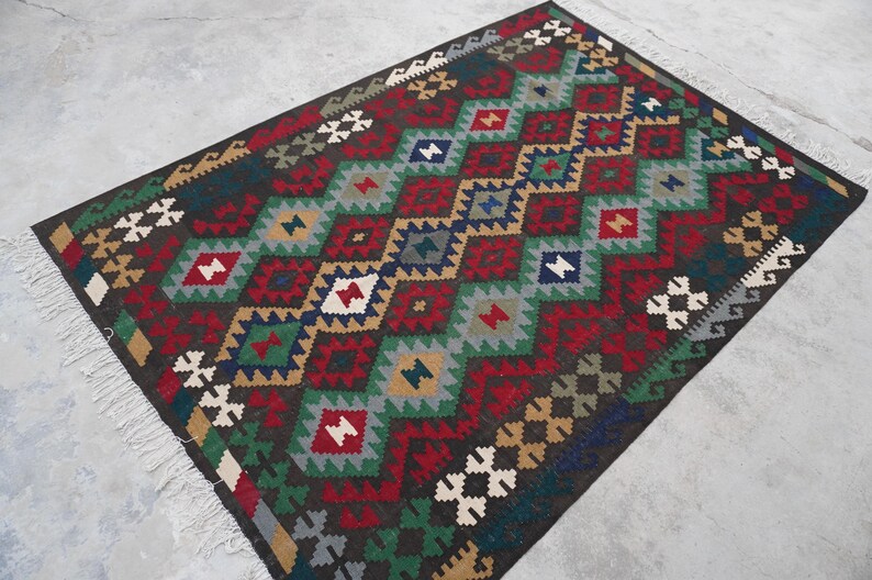 May include: A colorful rug with a geometric pattern in shades of red, green, blue, and brown. The rug has a diamond pattern with a fringe border.