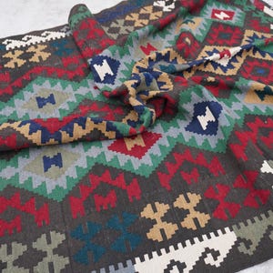 May include: A colorful rug with a geometric pattern in shades of red, green, blue, and brown. The rug is made of wool and has a hand-woven texture.