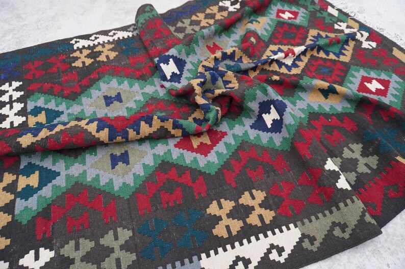 May include: A colorful rug with a geometric pattern in shades of red, green, blue, and brown. The rug is made of wool and has a hand-woven texture.