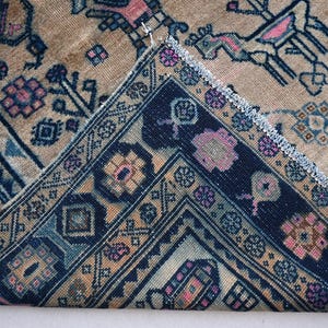 Peut inclure: Un tapis ancien avec un motif g&eacute;om&eacute;trique d&eacute;taill&eacute;. Le tapis pr&eacute;sente un fond beige avec des bordures bleu marine et des accents roses, bleus et bruns. Le design comprend des motifs floraux et animaliers, cr&eacute;ant une esth&eacute;tique vintage.