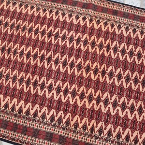 May include: A traditional rug with a geometric pattern in shades of red, black, and cream. The rug has a detailed border with a repeating motif.