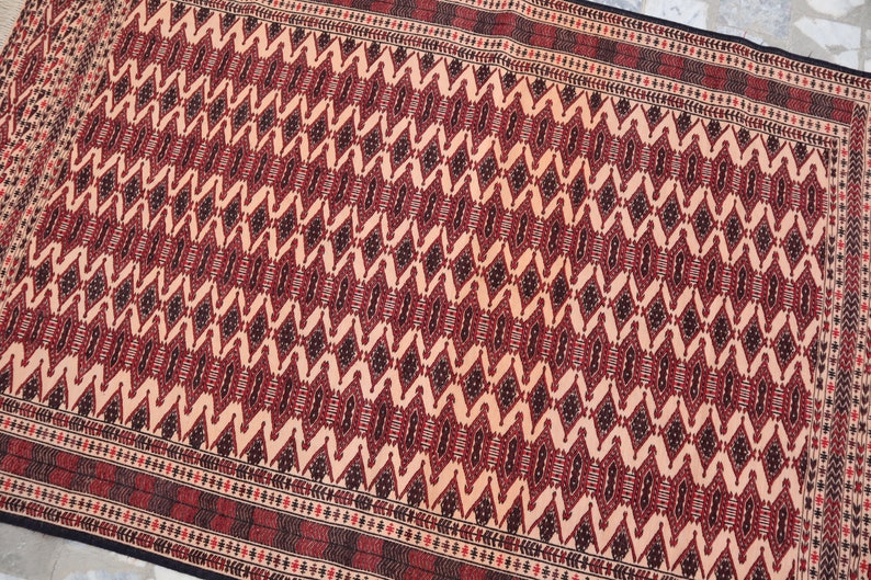 May include: A traditional rug with a geometric pattern in shades of red, black, and cream. The rug has a detailed border with a repeating motif.