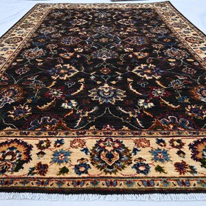 May include: A dark brown rug with a cream-coloured border. The rug features a floral pattern with intricate details. The rug has a fringe on the edges.