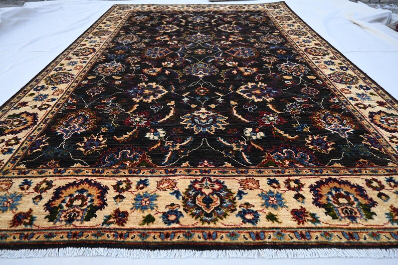 May include: A dark brown rug with a cream-coloured border. The rug features a floral pattern with intricate details. The rug has a fringe on the edges.