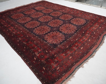 Puede incluir: Una alfombra rectangular con una paleta de colores rojo intenso y azul marino oscuro. El campo central muestra un patrón repetitivo de grandes medallones florales circulares, enmarcado por un borde detallado con motivos geométricos y flecos.