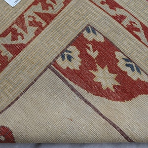 May include: Close-up of a beige rug with red, white, and blue geometric patterns. The rug has a woven texture and a fringe border.