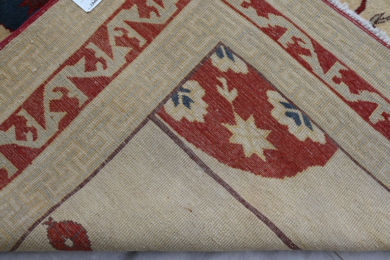 May include: Close-up of a beige rug with red, white, and blue geometric patterns. The rug has a woven texture and a fringe border.