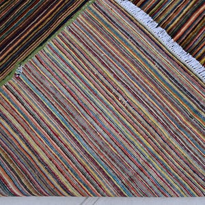 Pode incluir: Um tapete listrado multicolorido com franjas brancas. O tapete &eacute; feito de tecido tecido e tem um padr&atilde;o geom&eacute;trico.