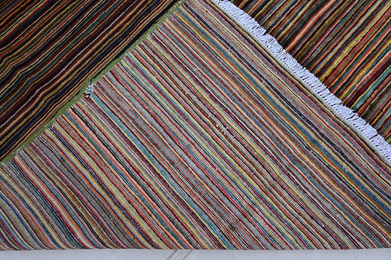 Pode incluir: Um tapete listrado multicolorido com franjas brancas. O tapete &eacute; feito de tecido tecido e tem um padr&atilde;o geom&eacute;trico.