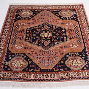 May include: Square, hand-knotted rug with a central medallion design. The rug features a navy blue and peach color palette with intricate geometric patterns and a fringed edge. The rug's dimensions are approximately 4 feet by 4 feet.