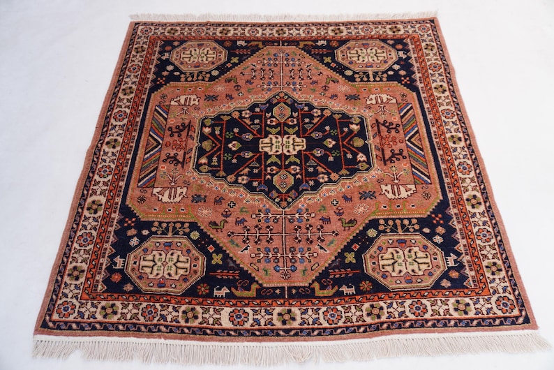 May include: Square, hand-knotted rug with a central medallion design. The rug features a navy blue and peach color palette with intricate geometric patterns and a fringed edge. The rug's dimensions are approximately 4 feet by 4 feet.