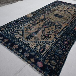 May include: A vintage rug with a blue and beige color scheme. The rug has a floral pattern with a central medallion. The rug is hand-woven and has a fringed edge.