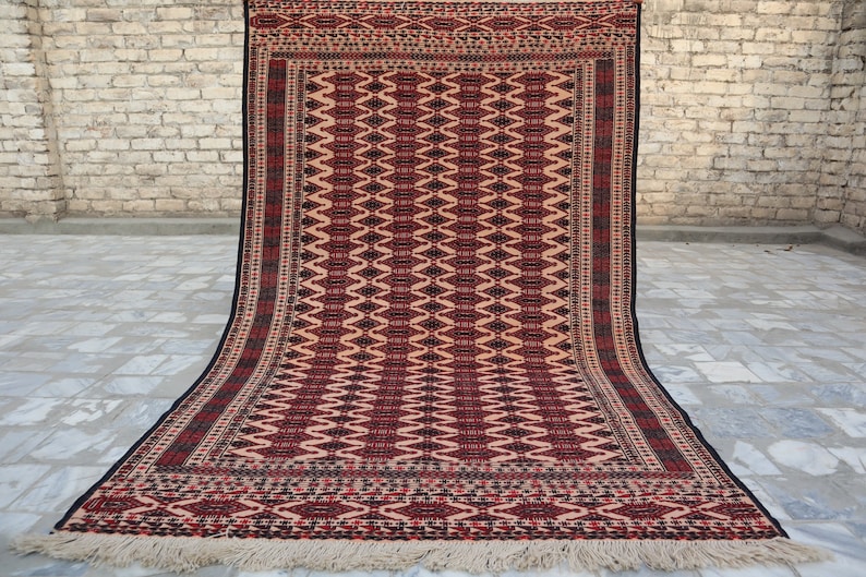 May include: A red, black and cream rug with a geometric pattern. The rug has a fringed border.