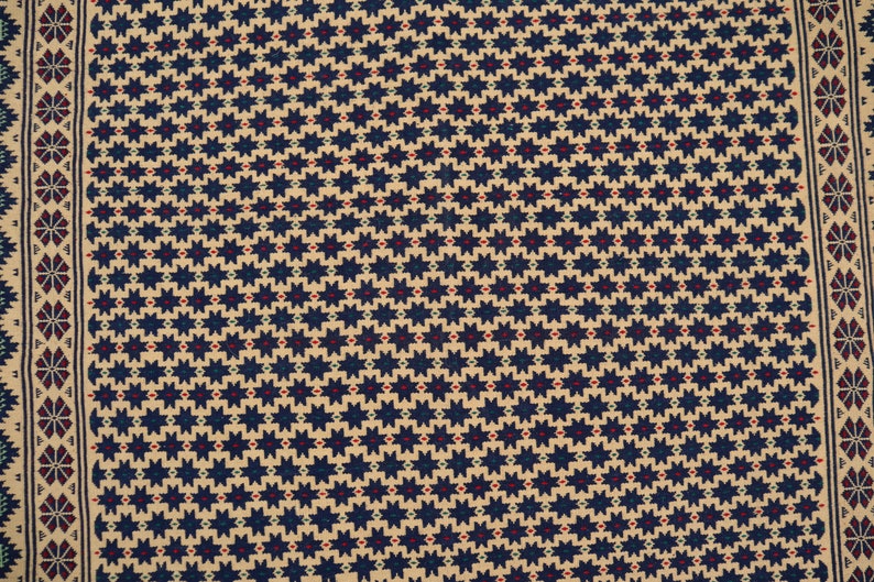 May include: A beige fabric with a repeating pattern of dark blue stars with red and green accents.