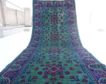 May include: A rectangular, hand-woven rug with a central green field and intricate patterns in blue and red. The rug features a detailed border and floral motifs, showcasing traditional craftsmanship. The rug's design is symmetrical, with a central medallion.