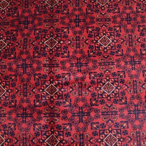 May include: A red rug with a repeating geometric pattern in black, white, and orange. The pattern features a central diamond shape surrounded by smaller geometric shapes.