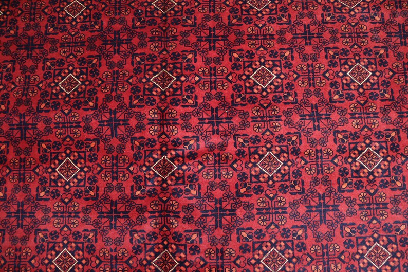 May include: A red rug with a repeating geometric pattern in black, white, and orange. The pattern features a central diamond shape surrounded by smaller geometric shapes.