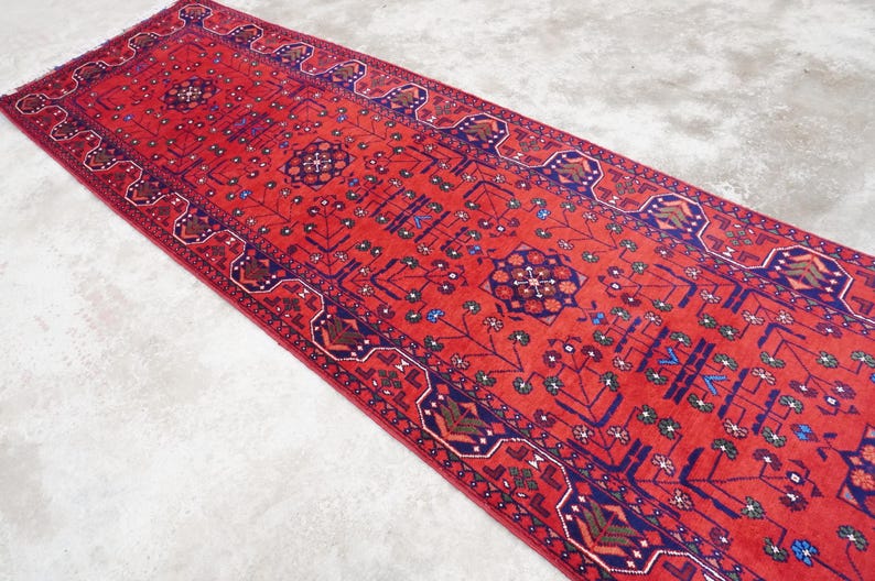 May include: A red runner rug with a traditional Persian design. The rug has a dark blue border with intricate patterns in shades of red, blue, and green.