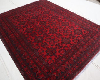 May include: A red rug with a dark blue intricate pattern. The rug has a fringed edge.