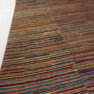 May include: A rectangular area rug featuring a dense, multi-colored horizontal striped pattern. The design consists of thin, repeating lines in shades of red, orange, yellow, blue, purple, and green, creating a vibrant, textured surface across the fabric.