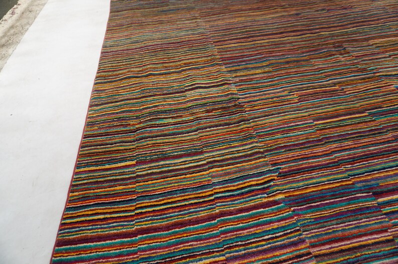 May include: A rectangular area rug featuring a dense, multi-colored horizontal striped pattern. The design consists of thin, repeating lines in shades of red, orange, yellow, blue, purple, and green, creating a vibrant, textured surface across the fabric.