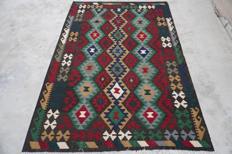 May include: A colorful rug with a geometric pattern in shades of red, green, blue, and brown. The rug has a fringe border.