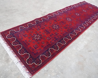 May include: A red runner rug with a blue and white geometric pattern. The rug has a fringe border.