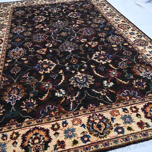 May include: A dark brown rug with a cream-coloured border. The rug has a floral pattern with intricate details in shades of blue, red, and green.