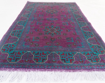 Könnte beinhalten: Rechteckiger Teppich mit tiefviolettem Feld und türkisfarbenem Rand. Der Rand weist geometrische Muster in Türkis, Rot und Braun auf. Weiße Fransen akzentuieren die Unterkante. Das Design des Teppichs ist symmetrisch.
