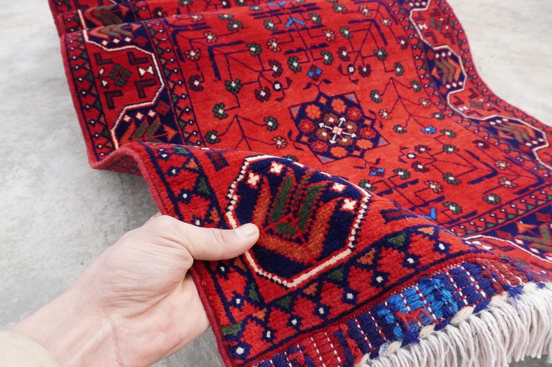 May include: A red, blue, and green patterned rug with a fringe border. The rug has a traditional design with geometric shapes and floral motifs.