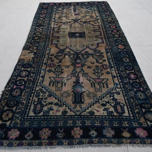 Peut inclure: Tapis rectangulaire beige et bleu marine avec un motif complexe. Le tapis pr&eacute;sente un motif central avec des motifs floraux et g&eacute;om&eacute;triques, encadr&eacute; par une bordure bleu marine avec des accents floraux. Le design du tapis est sym&eacute;trique.