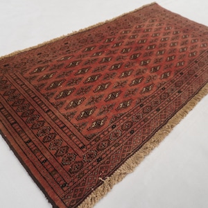 May include: A rectangular area rug featuring a deep red base color with a repeating pattern of dark brown and cream diamond-shaped motifs. The rug includes intricate geometric borders and a light tan fringe along the two shorter edges.