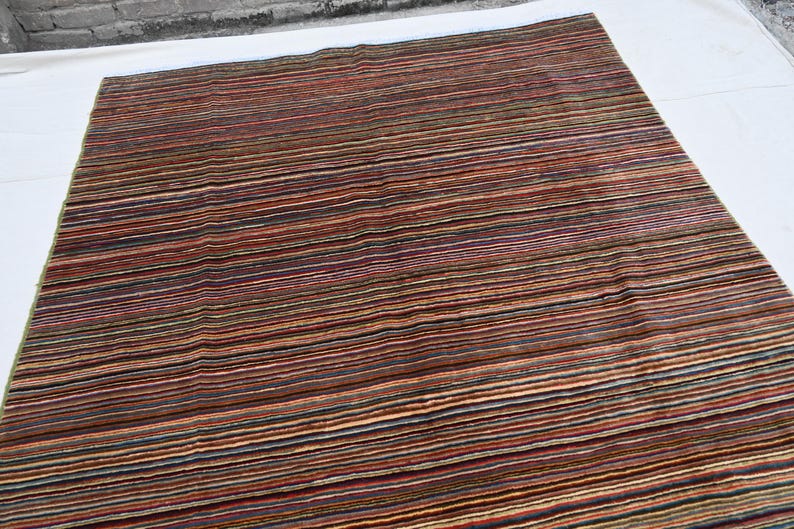 Pode incluir: Um tapete listrado multicolorido com uma variedade de tons de marrom, vermelho, verde e bege. O tapete tem um design contempor&acirc;neo e &eacute; feito de um material macio e felpudo.