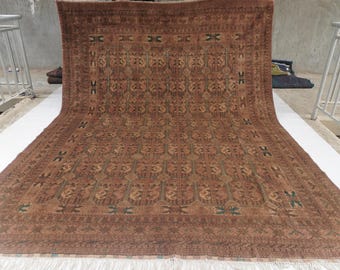 May include: A large rectangular area rug featuring a deep brown base color with a repeating geometric pattern in lighter tan and dark green accents. The rug has a wide decorative border and a white fringe along the bottom edge of the textile.