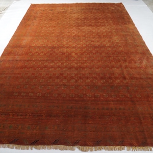 Könnte beinhalten: Ein großer rechteckiger Teppich in einem tiefen gebrannten Orangeton mit einem sich wiederholenden Muster aus kleinen geometrischen Motiven, die in horizontalen Bändern über die Fläche angeordnet sind, abgeschlossen mit kurzen hellen Fransen.