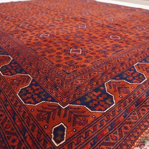 May include: A traditional Persian rug with a red background and intricate blue and green patterns. The rug has a fringed edge.