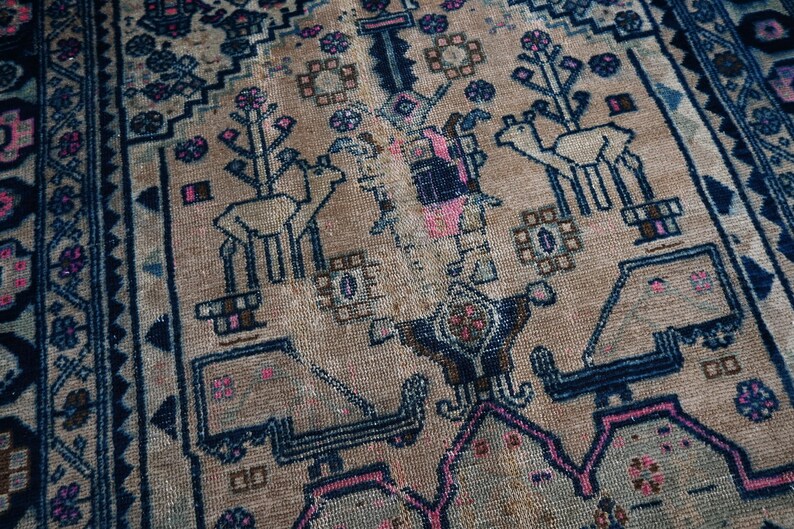 May include: A vintage rug with a beige background and intricate blue and pink patterns. The rug features a repeating design of stylized trees and animals.