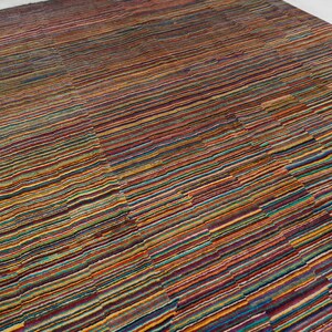 May include: A rectangular area rug featuring a dense, multi-colored striped pattern. The design consists of thin, horizontal lines in various shades of red, orange, yellow, blue, green, and purple, creating a vibrant, textured appearance across the surface.