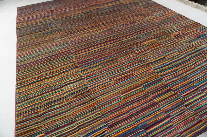May include: A rectangular area rug featuring a dense, multi-colored striped pattern. The design consists of thin, horizontal lines in various shades of red, orange, yellow, blue, green, and purple, creating a vibrant, textured appearance across the surface.