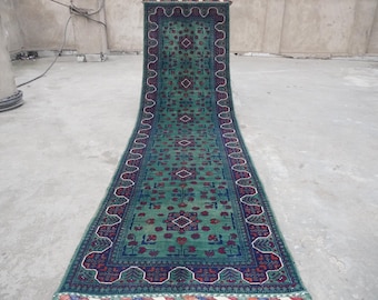 May include: A long, green runner rug with a traditional Persian design. The rug has a dark blue border with red and white accents.