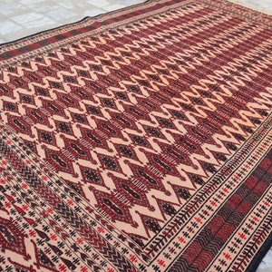 May include: A traditional rug with a geometric pattern in shades of red, black, and cream. The rug has a fringed border.